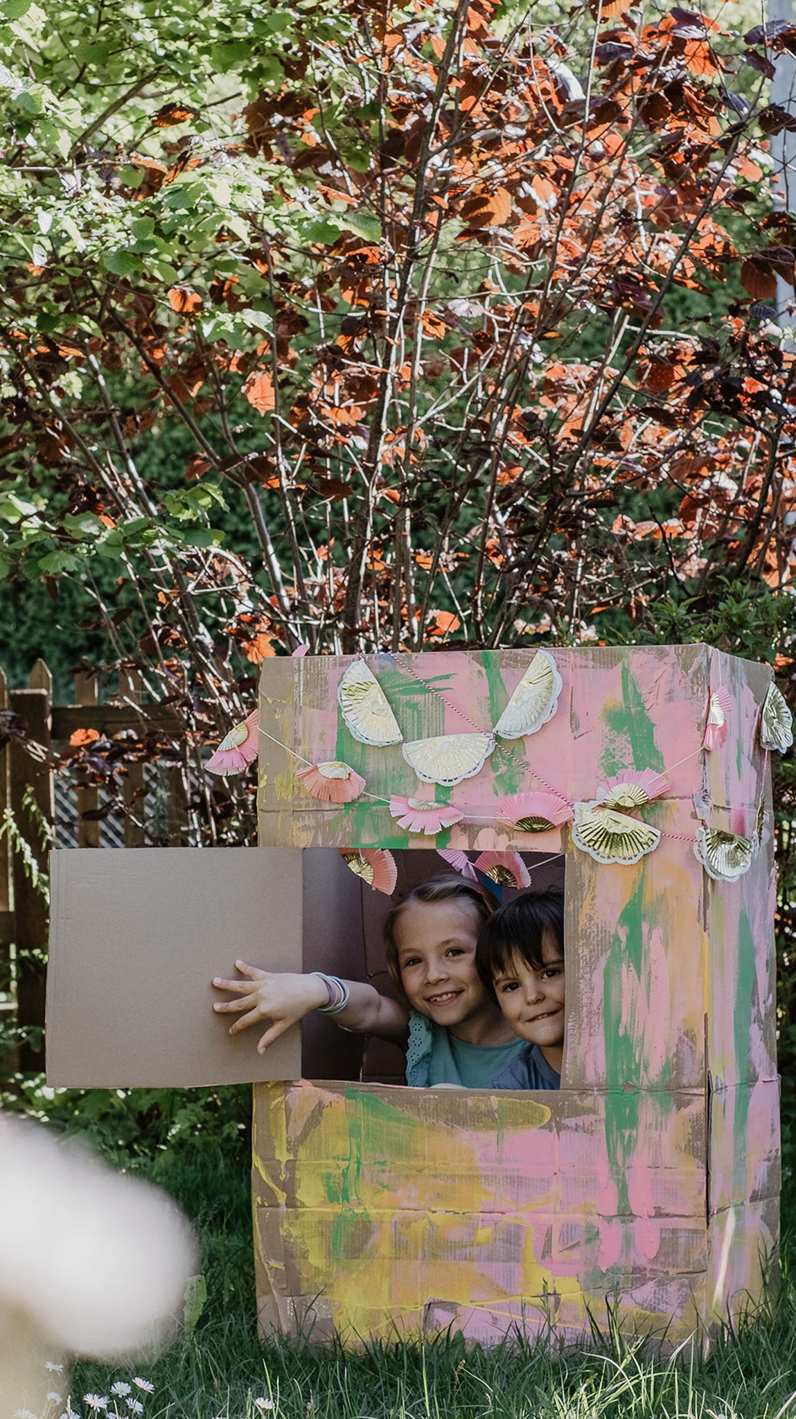 Kinder spielen mit Kartonhaus im Garten